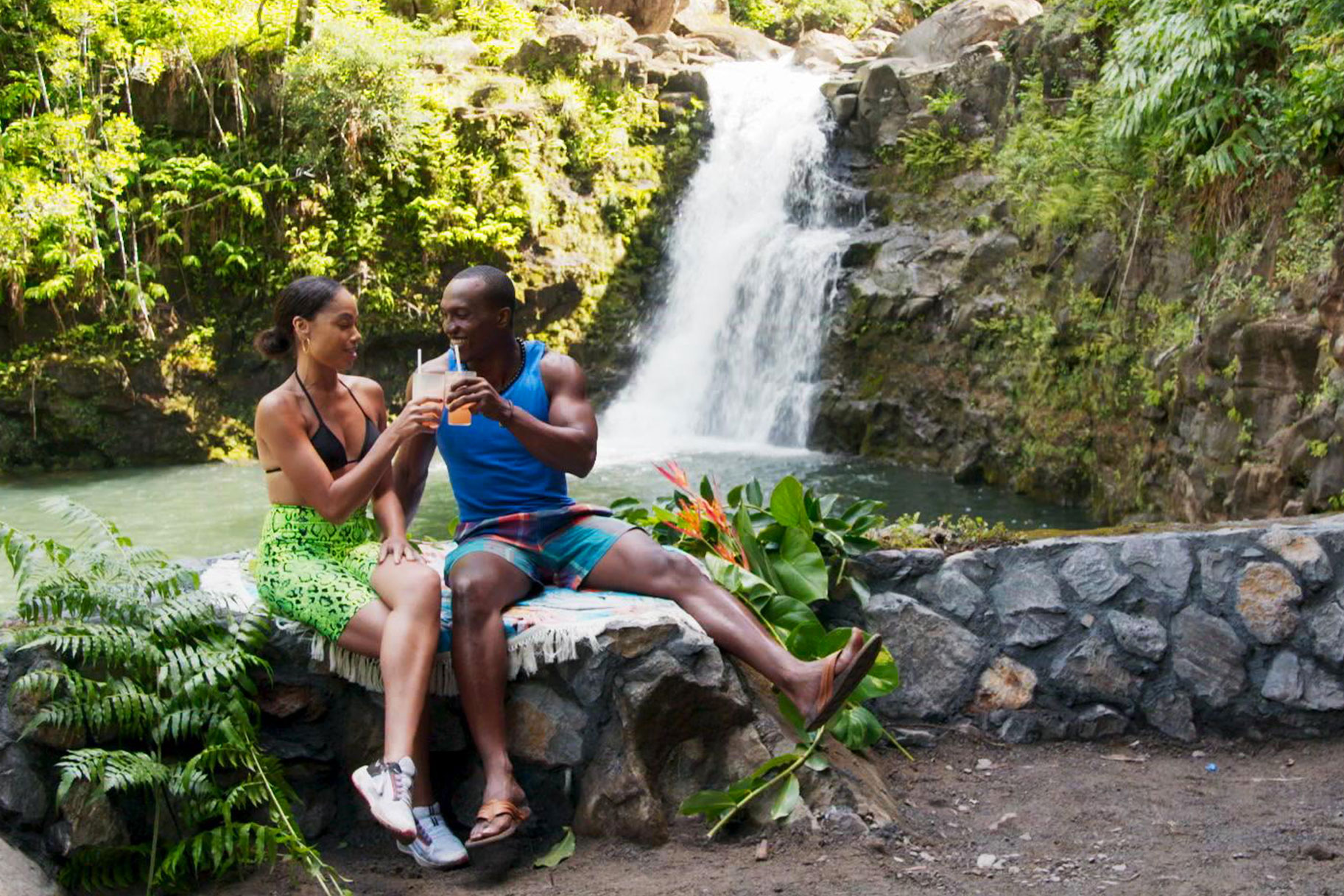 Ashely and Evan on a date, drinking cocktails in front of a waterfall