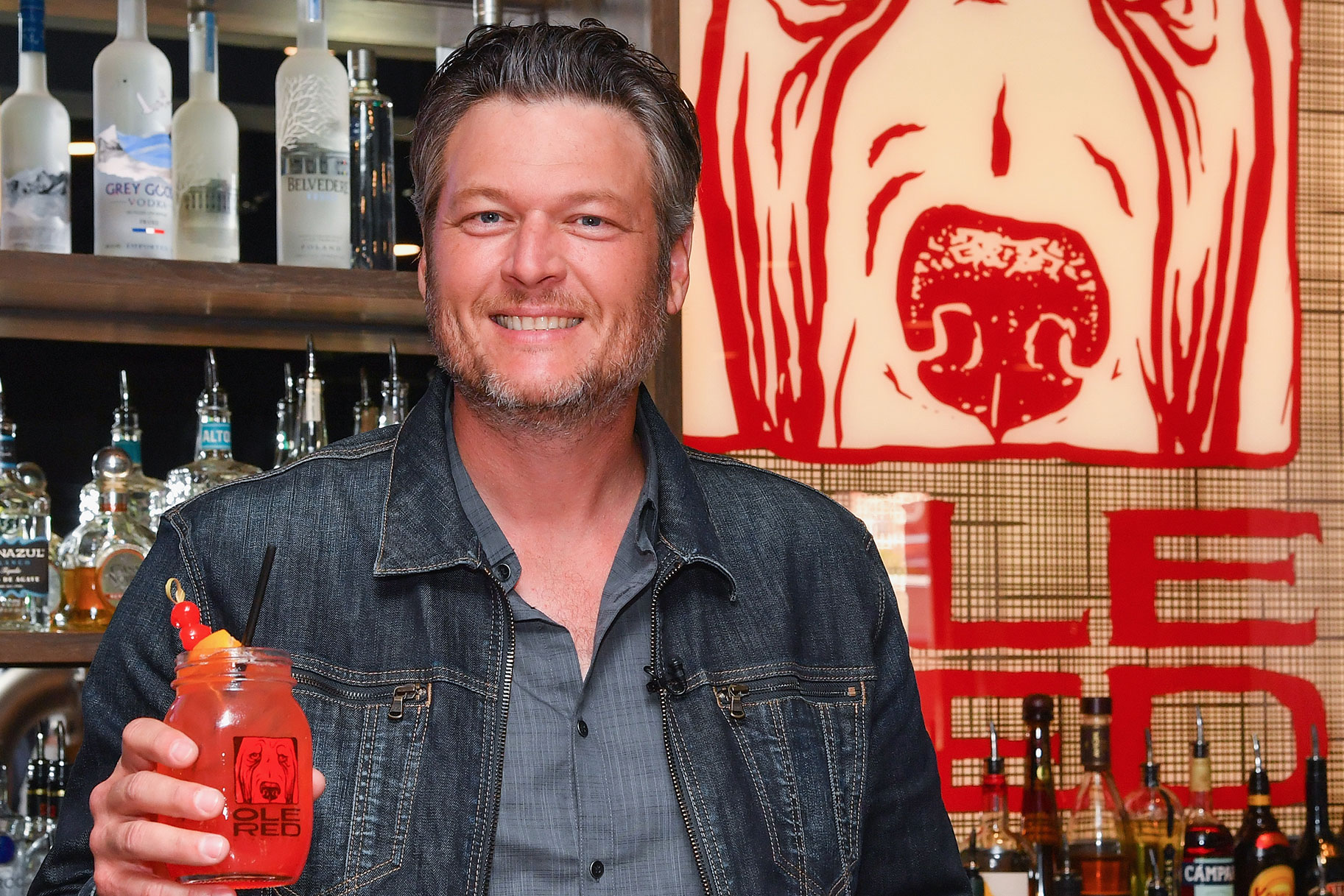 Blake Shelton holding a mixed drink in front of a bar