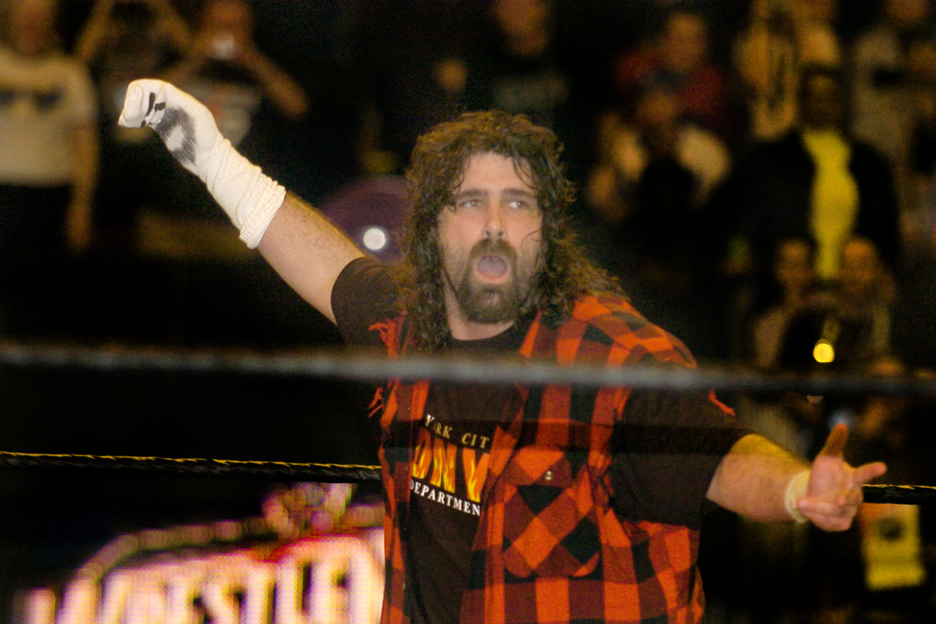 Mick Foley with his arms outstretched in the ring, wearing a sock on his right hand