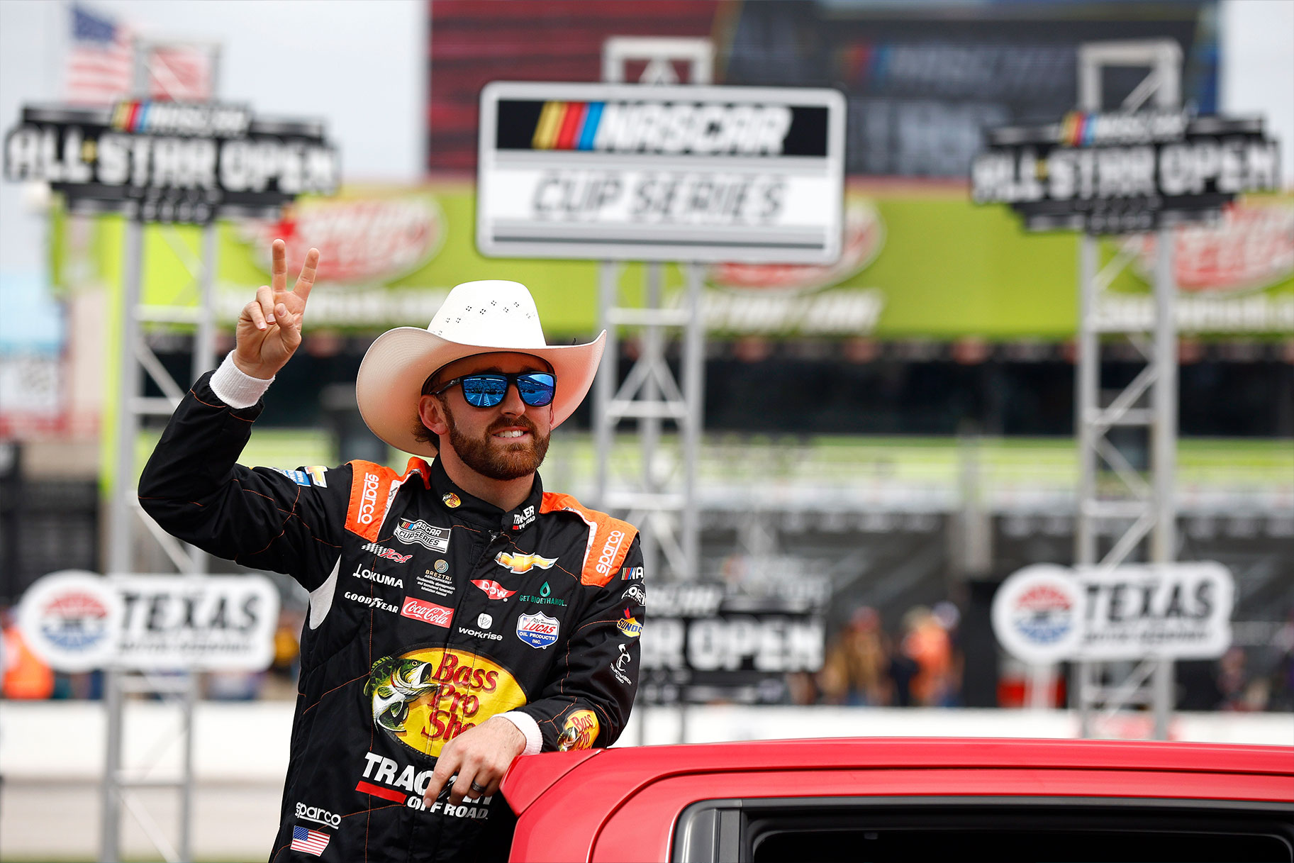Austin Dillon leaning on his racecar while wearing a cowboy hat and sunglasses