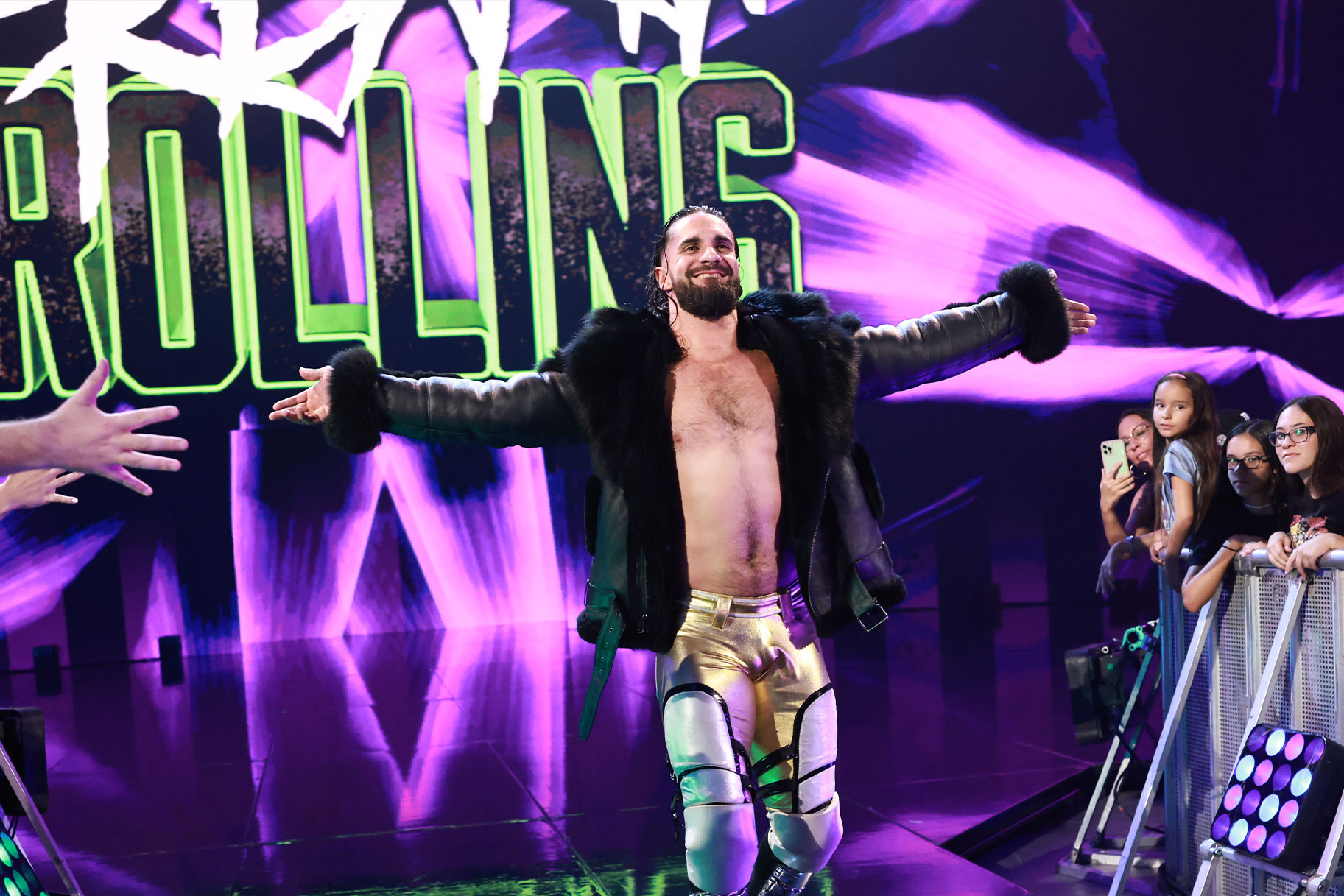 Seth Rollins walking to the ring with his arms extended and a smile on his face