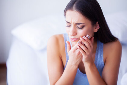 Woman sitting on bed holding the side of her mouth in pain