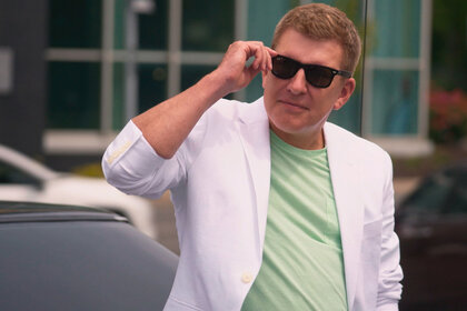 Todd Chrisley adjusting his black sunglasses while wearing a lime green shirt and white blazer jacket
