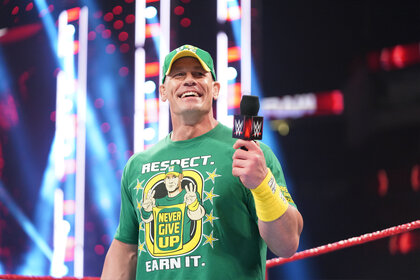 Wrestler John Cena in a green shirt and hat holding a mic