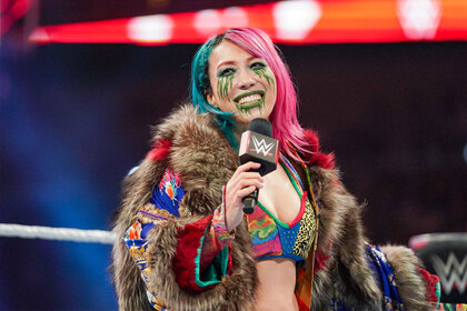 Asuka standing in the ring, smiling while holding a mic in her hand