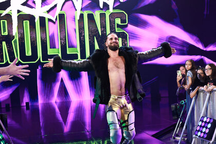 Seth Rollins walking to the ring with his arms extended and a smile on his face