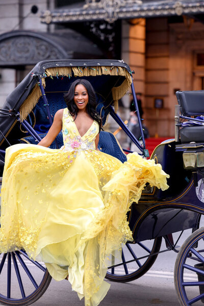 Nicole Remy standing in front if a carriage wearing a yellow gown