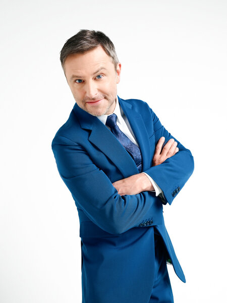 Chris Hardwick wearing a blue suit in front of a white backdrop.