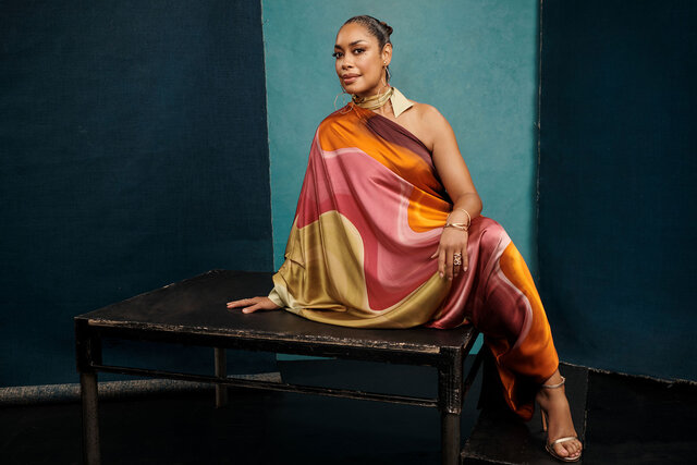 Gina Torres poses while sitting on top of an old table