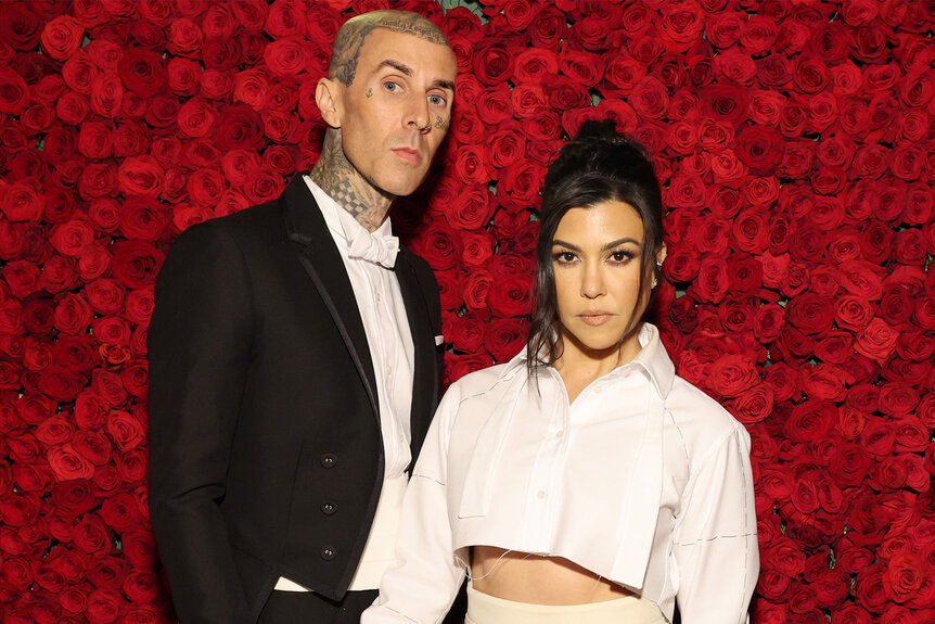 Kourtney Kardashian and Travis Barker posing together in front of a wall of roses