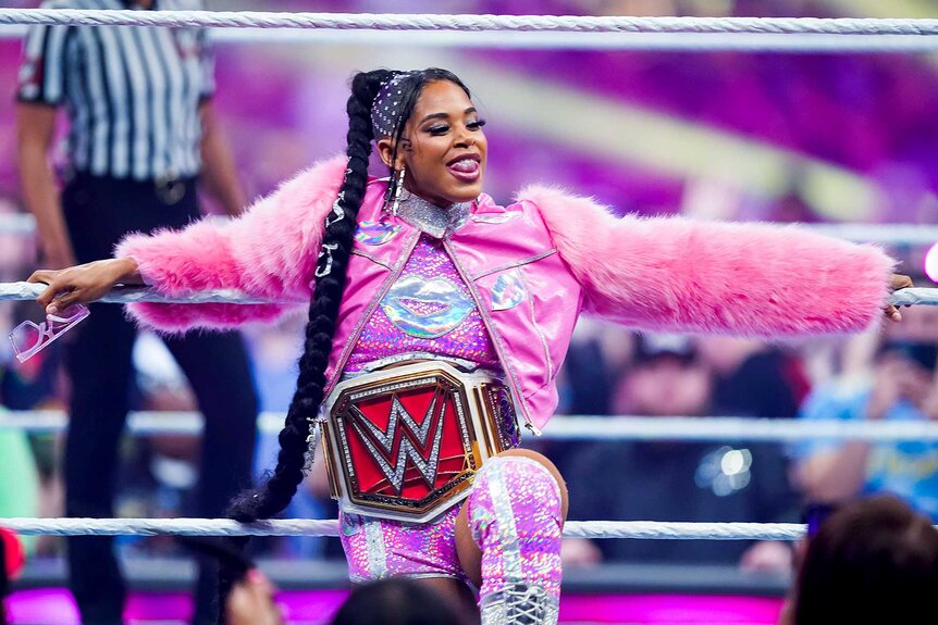 Bianca Belair sticks her tongue out in a pink outfit in the ring