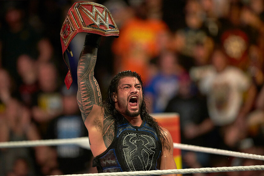 Roman Reigns lifts his belt above his head in a moment of passion