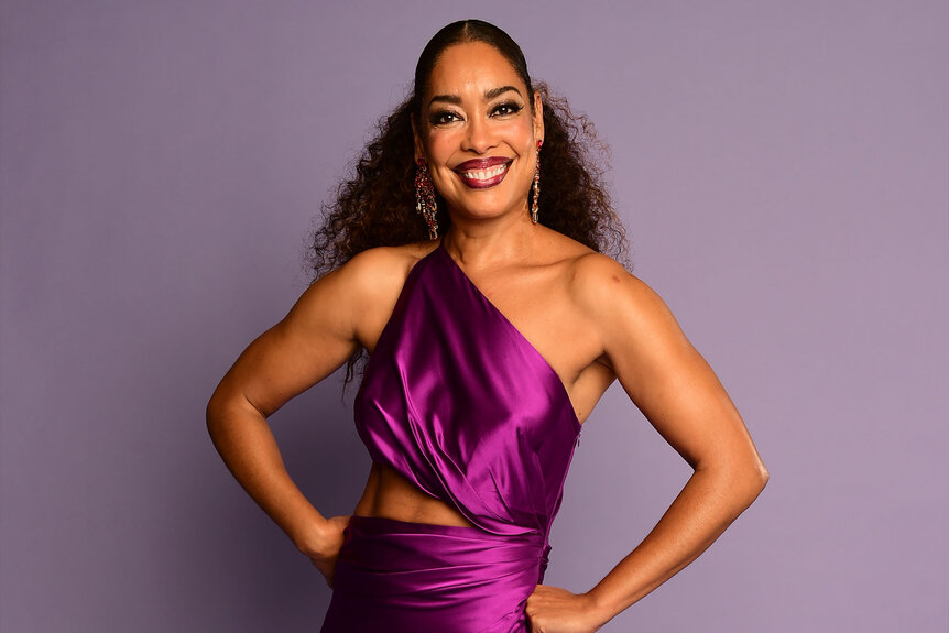 Gina Torres poses for a photo in a purple one shoulder dress