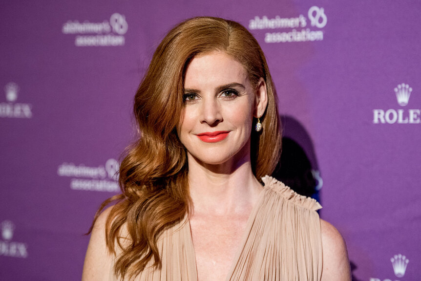 Close up of Sarah Rafferty in front of a purple backdrop on a red carpet