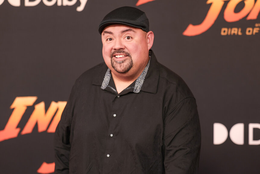Gabriel Iglesias wearing a black button up shirt and black cap on the arrivals carpet for "Indiana Jones and the Dial of Destiny" premiere.