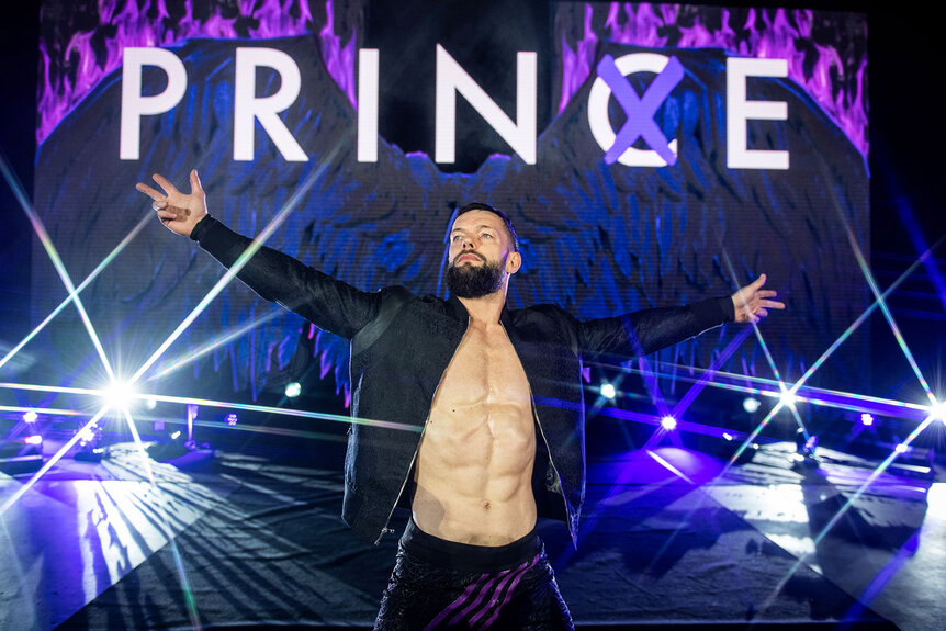 Finn Balor poses wikth his arms oujtstretc hed while walking towards the ring.