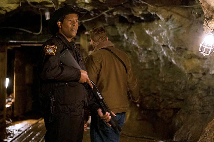 Resident Alien 409 Sheriff Mike Thompson in a cave holding a weapon